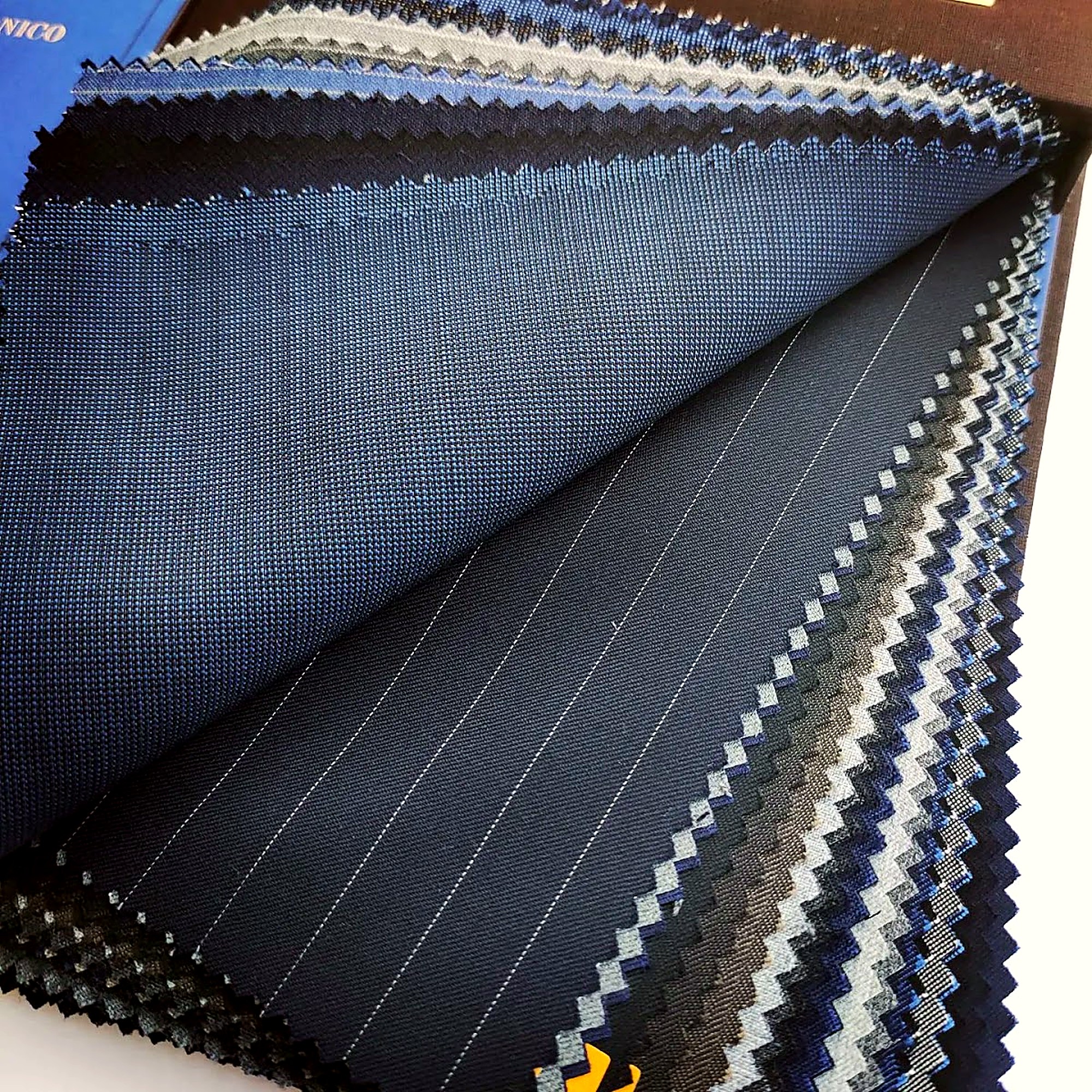 Several swatches of dark blue fabric for suits are displayed, with some featuring subtle pinstripes